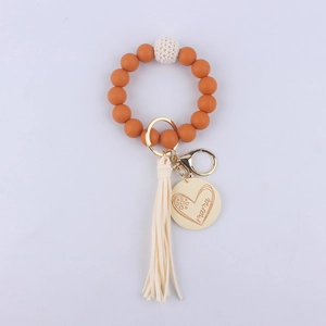 Detail of orange silicone wristlet keychain with wooden mama charm and cream tassel
