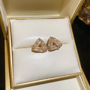 Macro shot of gold geometric triangle stud earrings with sparkling zircon on a cream case