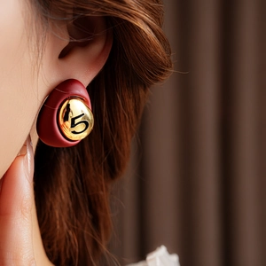 Macro view of vintage style deep red and gold number 5 stud earrings worn by a model