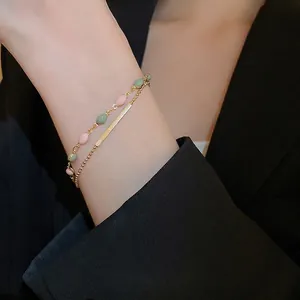 Double-layered gold-plated bracelet with pink and green oval beads on a model's wrist