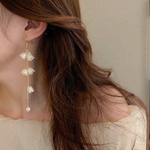 Gros plan de boucles d'oreilles muguet avec fleurs blanches et perles sur le modèle