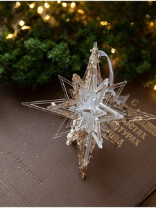 Close-up of a 3D star acrylic Christmas ornament with gold sequins and white ribbon
