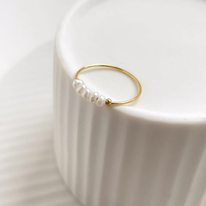 Macro detail of French style gold ring with five white pearls on white ceramic base