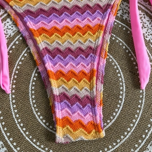 Detail of chevron knit bikini bottoms with pink side ties on a textured mat background
