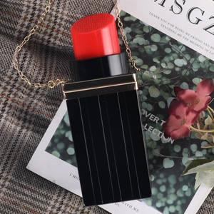Detail of a lipstick-shaped black evening clutch with red top and gold chain shoulder strap