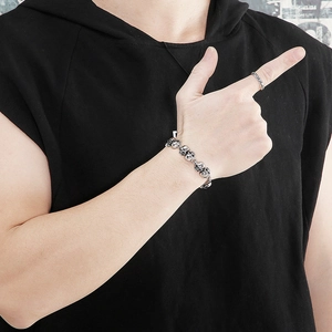 Close-up of men's vintage silver skull bracelet worn by a model against black fabric