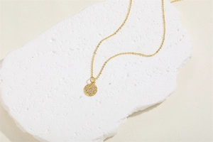 Detailed view of gold necklace with star zircon pendant on a white textured stone