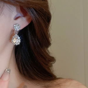 Close-up of sparkling floral stud and teardrop crystal earrings worn by a model