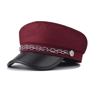 Detail of red fabric newsboy hat with black leather brim and double silver chains