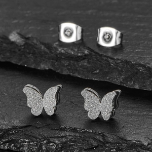 Sparkly silver butterfly stud earrings with glitter finish on black stone background