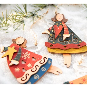 Close-up of painted wooden angel Christmas ornaments on snow and pine branches