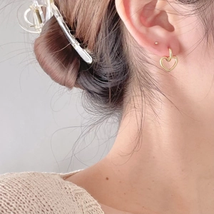 Close-up of a gold hollow heart stud earring worn on model ear to show size and style