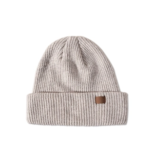 Detail shot of the chunky knit texture and brown leather patch on an oatmeal beanie