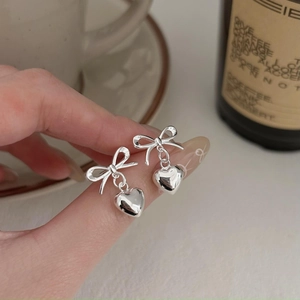 Elegant 925 sterling silver bow and heart dangle earrings held by a model for scale