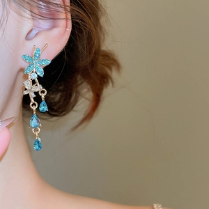Close-up of gold flower earrings with teal rhinestones and elegant teardrop tassels