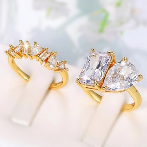 Elegant gold pear and rectangle cut cubic zirconia cluster rings on a white jewelry stand