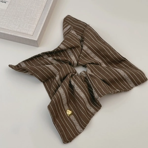 Détail d'un chouchou en tissu à rayures marron avec un médaillon doré en forme de cœur
