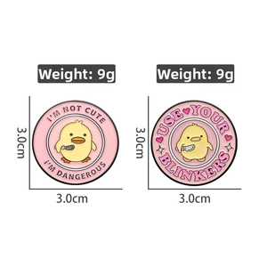 Detail view of pink enamel pins featuring cartoon yellow duck with knife and size specs