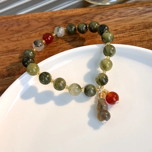 Detail of green stone bead bracelet with carnelian accents and a small jade gourd charm
