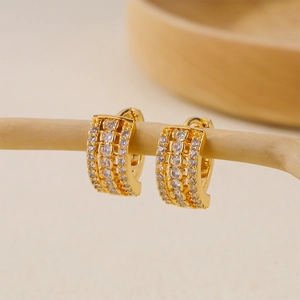 Close-up of gold huggie earrings with triple-row cubic zirconia on a wooden branch
