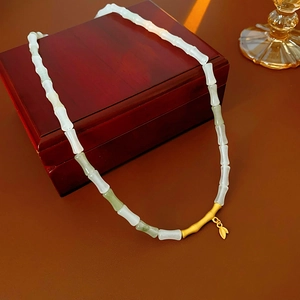 Detailed view of bamboo leaf necklace with jade-style beads and golden accents on wood