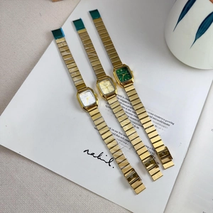 Detailed top view of three elegant square women's quartz watches with colored dials on a book