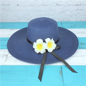 Detail of navy wide brim straw hat with black bow and plumeria flowers on wooden background
