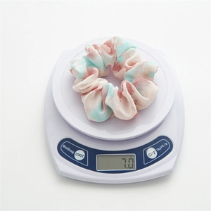 Detail showing a lightweight floral tie-dye scrunchie weighing 7.0g on a digital scale