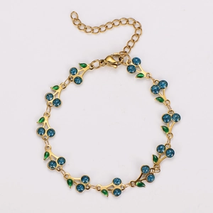 Detailed shot of bohemian gold chain bracelet with blue glitter cherry and green enamel leaf