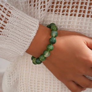 Macro shot of green marble-textured beaded bracelet worn on wrist with white knitwear
