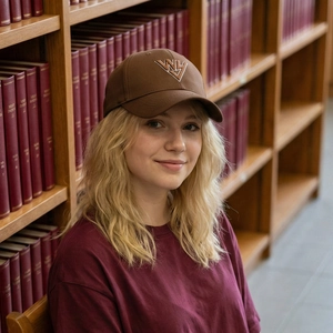 Braune Baumwoll-Baseballkappe mit WY-Stickerei, getragen von einem Modell in einer Bibliothek