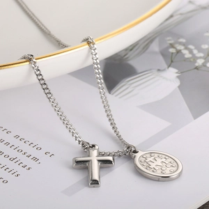 Close-up of silver steel necklace with cross and oval coin pendants on book page