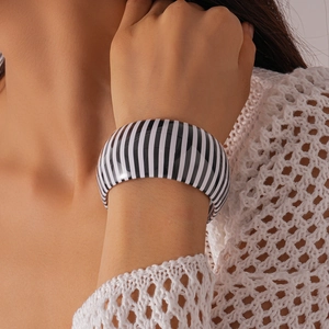 Dettaglio di un ampio bracciale in acrilico a righe bianche e nere indossato al polso
