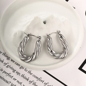 Dettaglio di orecchini a cerchio ovali intrecciati argento su vassoio in ceramica