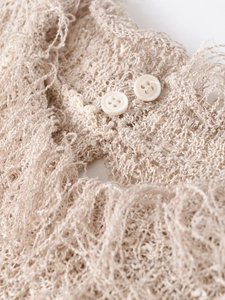 Nahaufnahme einer beigen Strickweste mit dekorativen Knöpfen und weichen Fransendetails