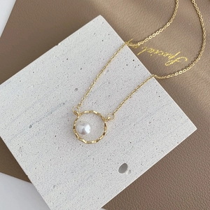 Minimalist geometric pearl necklace featuring a hammered gold circle pendant on a chain