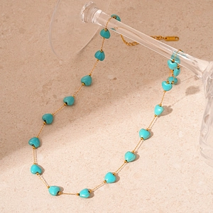 Détail macro du collier en acier doré avec perles de cœur turquoise sur pierre