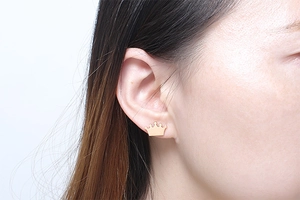 Detailed close-up of a stylish gold crown stud earring worn on a female model ear