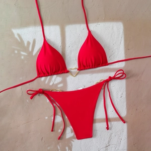 Detail of red bikini with golden heart rings and side-tie briefs on shadow background
