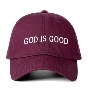Detail of white God Is Good embroidery on a burgundy cotton baseball cap with ventilation holes