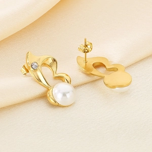 Close-up of gold heart earrings with white pearls and crystals on beige silk fabric