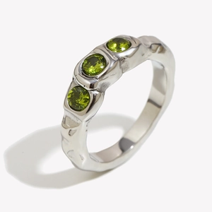 Polished silver ring with three green zircons and irregular texture at a 45-degree angle