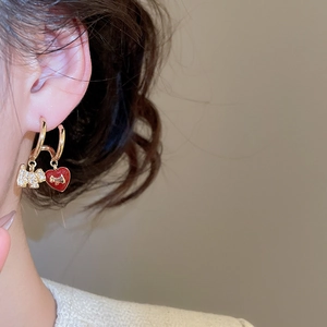Close-up of gold-plated puppy stud earring with zircon and red heart on model ear