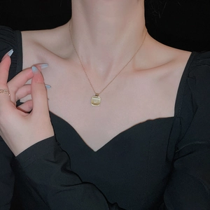 Gros plan d'un collier doré avec pendentif carré œil-de-chat porté avec élégance au cou