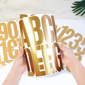 Hand holding 5 inch gold foil letter sticker showing large size and metallic texture