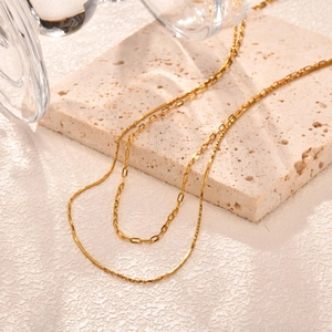 Double-layered gold snake and paperclip chain necklace on a textured stone surface