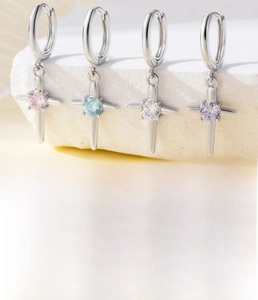 Macro detail of cross earrings featuring colorful cubic zirconia on a white stone background