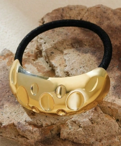 Macro shot of gold metallic hair tie with irregular textured surface on stone background