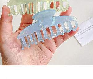Detail view of light blue and green iridescent crescent hair claws held by a hand