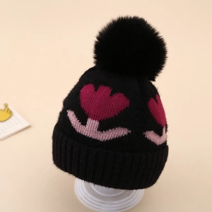 Close-up of knit baby beanie with floral patterns and large faux fur pompom detail